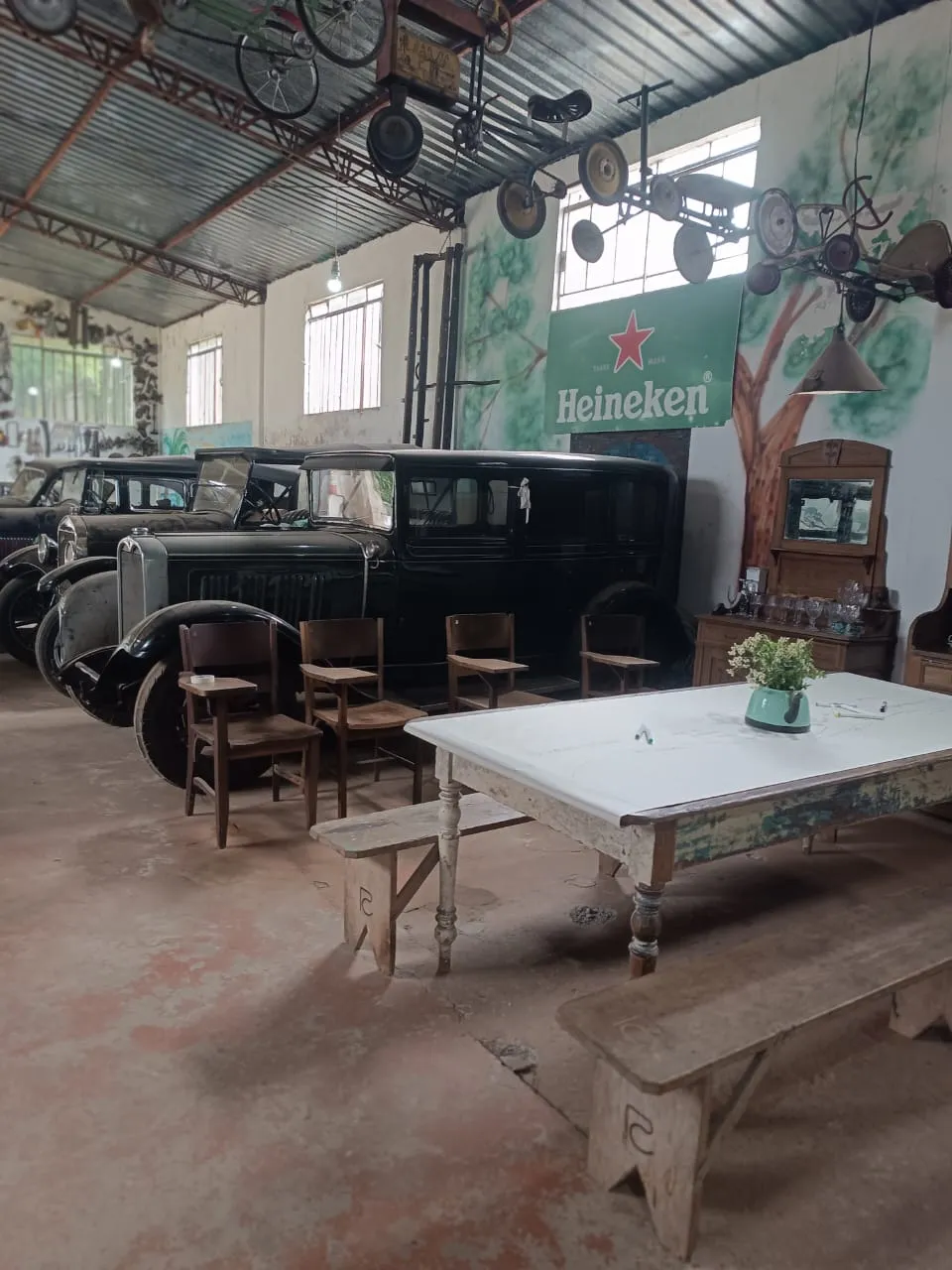 Carros antigos estacionados em uma ampla garagem rústica com mesa e um letreiro vintage